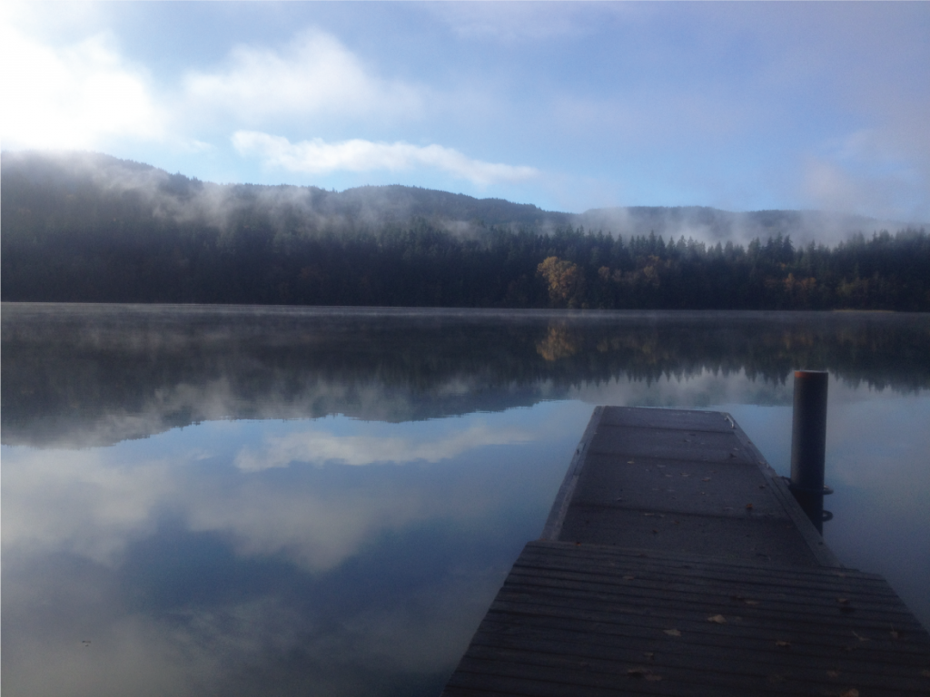 The dock over placid Lake Padden, with clouds reflected in the water's surface.
